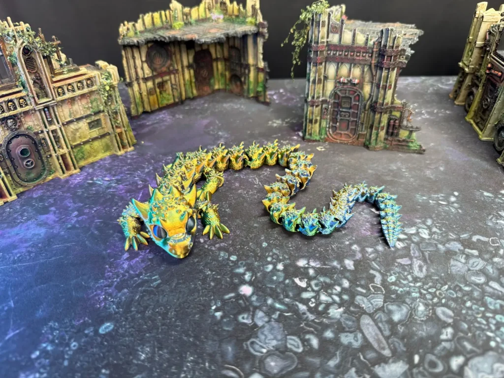 Photo of a 3d printed dragon presented on a playmat with terrain features in the backdrop.